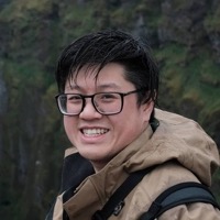 Hoye Lam, lachend in een regenjas boven een groene kloof
